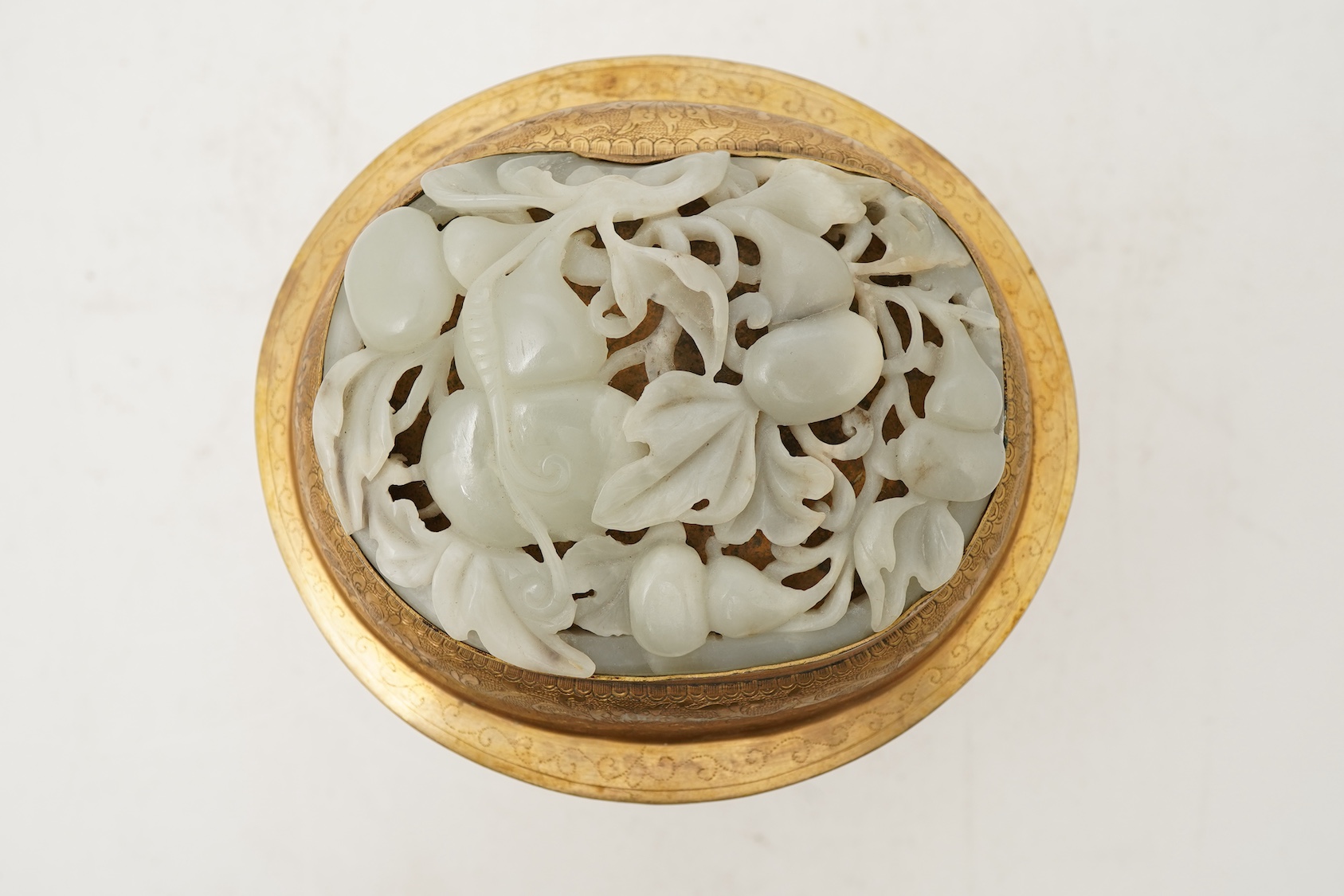 A Chinese pale celadon jade oval plaque, 17th/18th century, mounted on a late Qing gilt copper jar